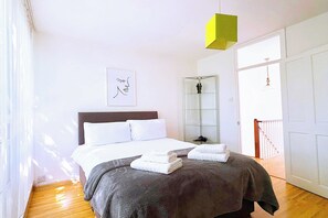 A bedroom with a bed, a bedside table, a mirror, and a window.
