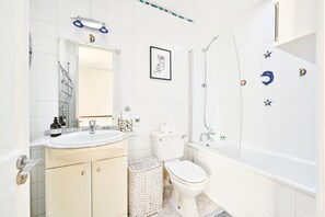 A bathroom with a white sink, toilet, and bathtub. There is a framed picture on the wall and a small basket next to the toilet.