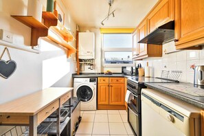 A compact kitchen with wooden cabinets, a washing machine, a dishwasher, and a stove.