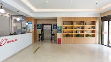 Ein Hotel-Empfangsbereich mit Empfangstresen, einem Holzbücherregal und freiem Blick auf den Aufzug.