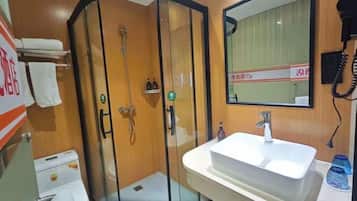 Casa de banho de hotel com chuveiro em cabine de vidro, pia e espelho.