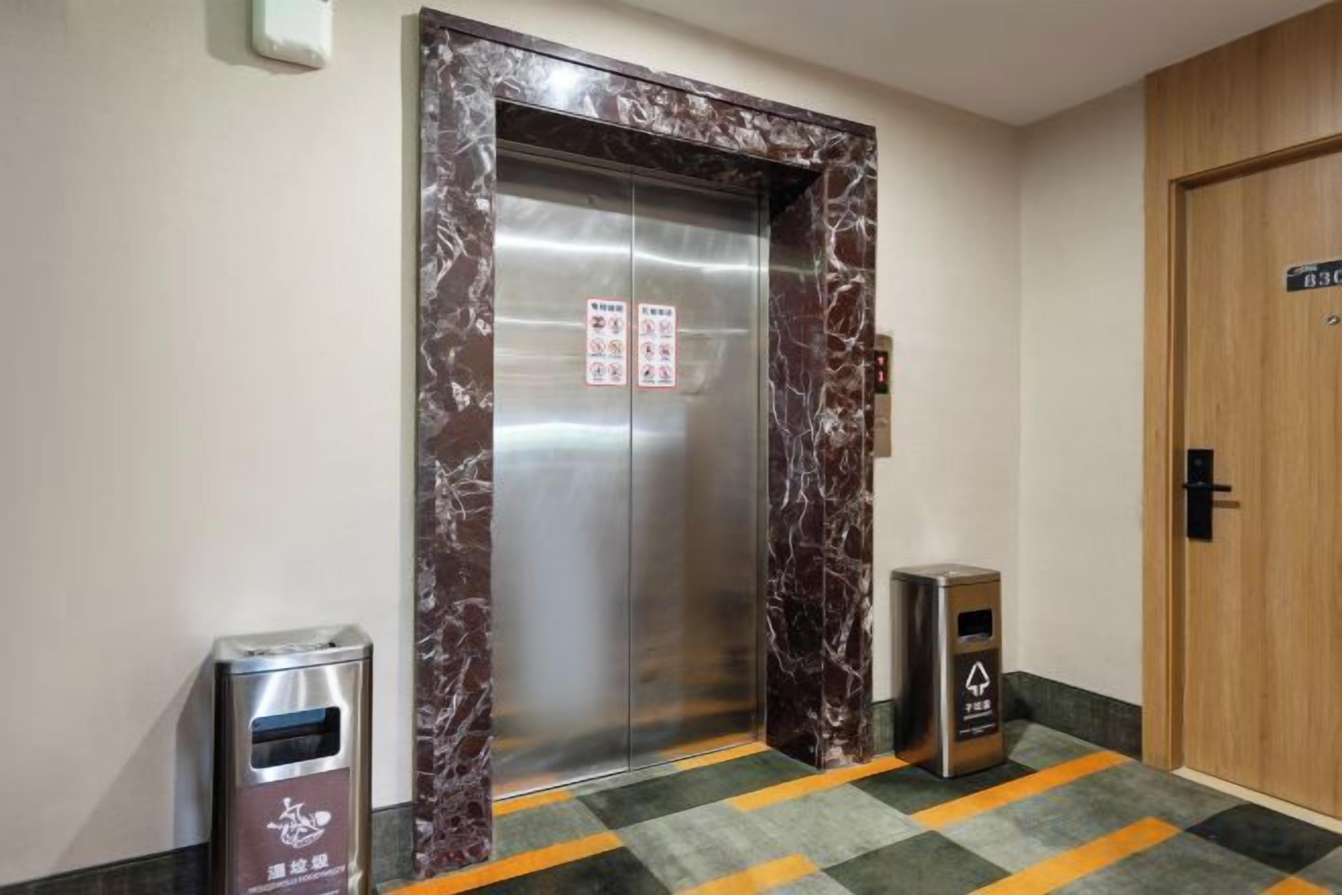 An elevator with a marble frame, a trash bin, and a door with a sign.