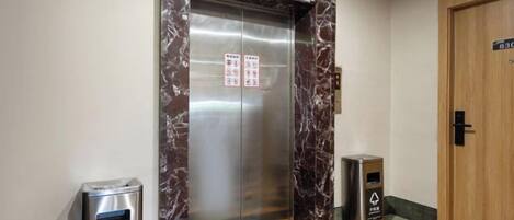 An elevator with a marble frame, a trash bin, and a door with a sign.