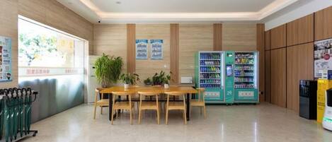A reception area with a wooden reception desk, a green vending machine, and a bulletin board with notices.