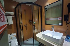 Egy szállodai fürdőszoba, melyben üvegfalas zuhanyzó, tükörrel ellátott mosdókagyló és WC található.