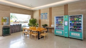 Un espace intérieur moderne avec une table et des chaises en bois, des distributeurs automatiques et des affiches d’information accrochées aux murs.