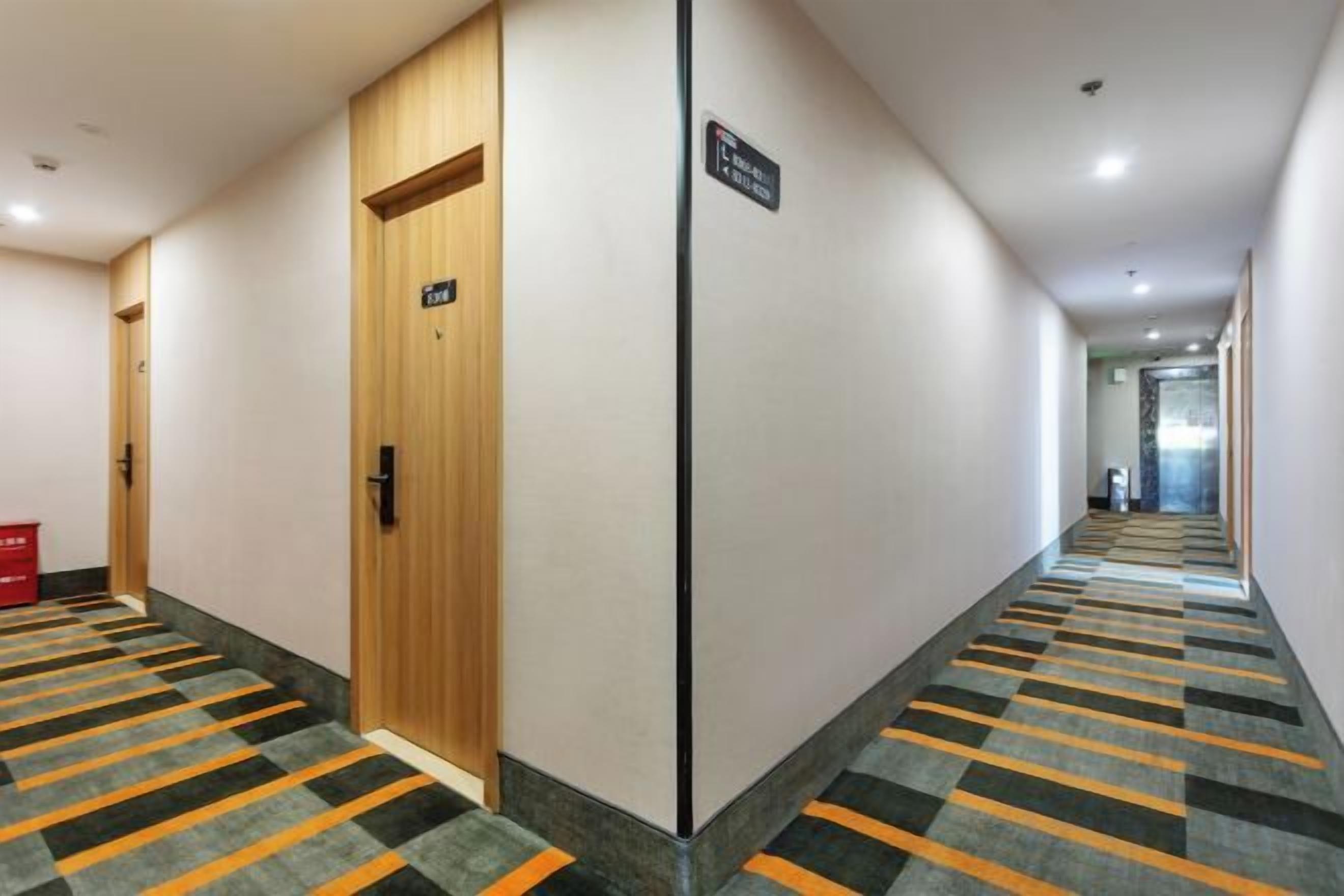 A hotel corridor with carpeted floors, wooden doors, and a sign indicating the direction to the elevator.
