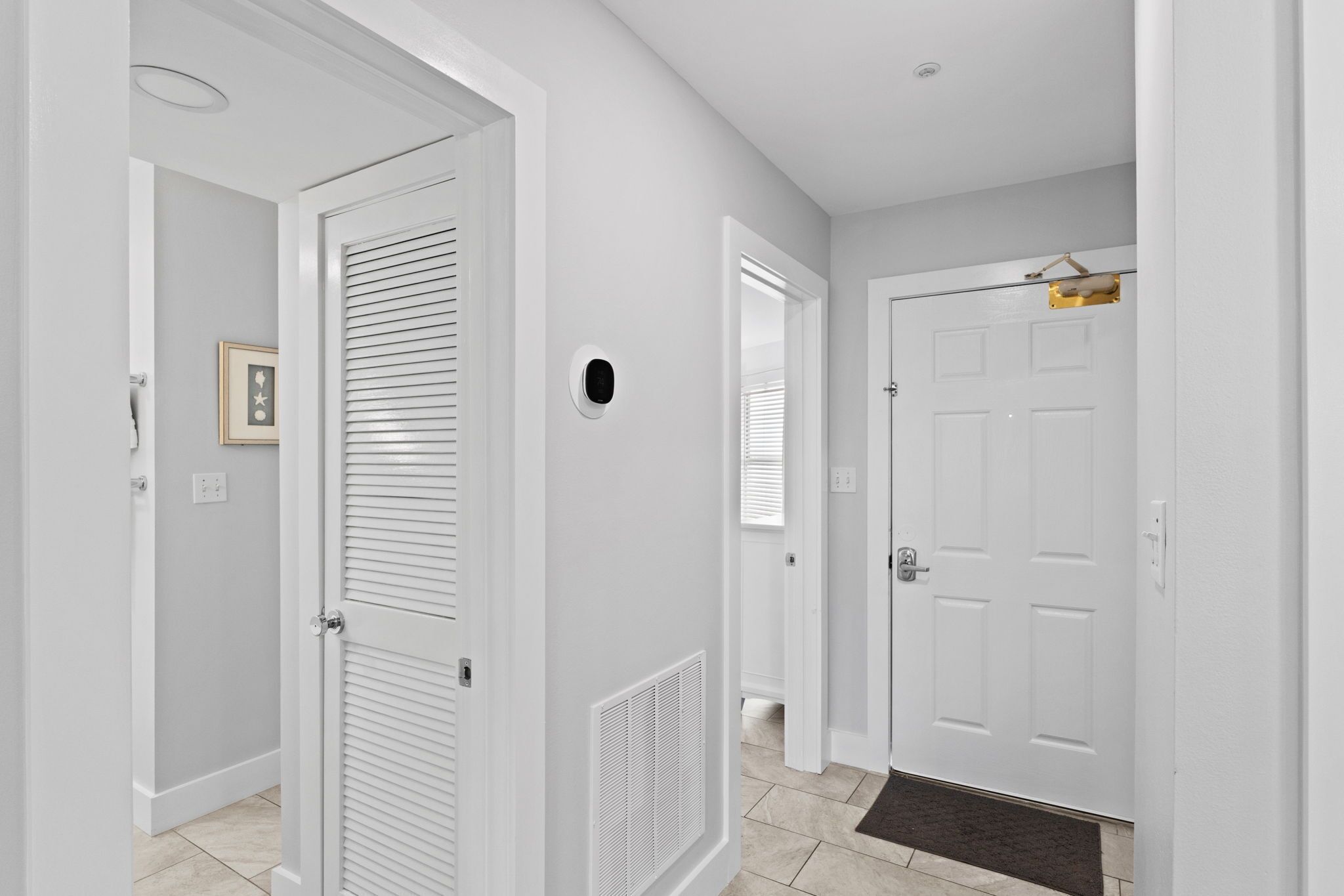 A hallway with white doors, a vent, and a framed picture on the wall.