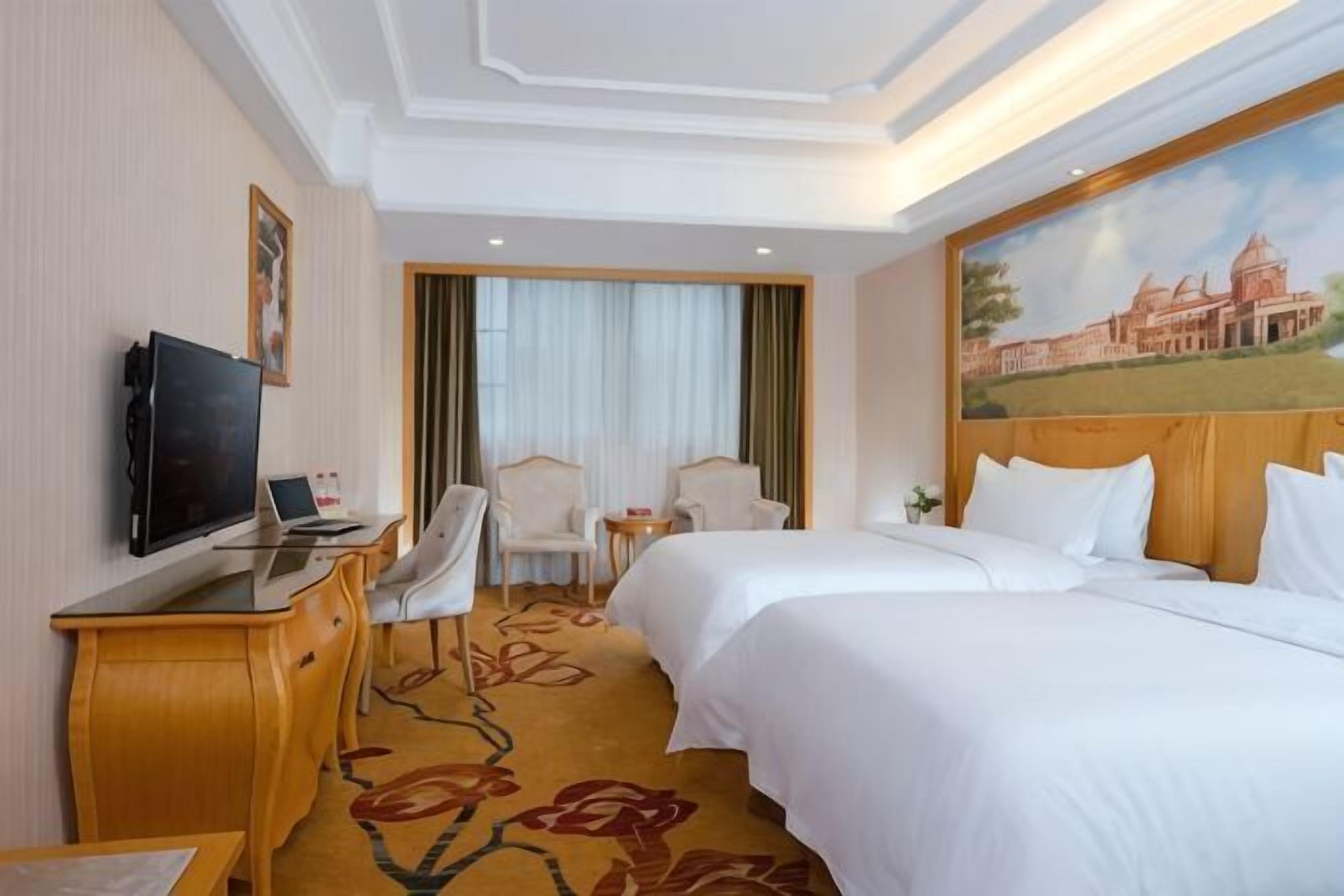 Una habitación de hotel con una cama, un escritorio con televisor, una silla y un cuadro en la pared.