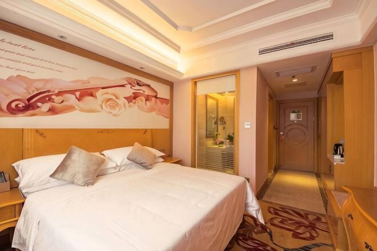 A hotel room with a large bed, a wooden headboard, a wall mural, a mirror, and a carpeted floor.