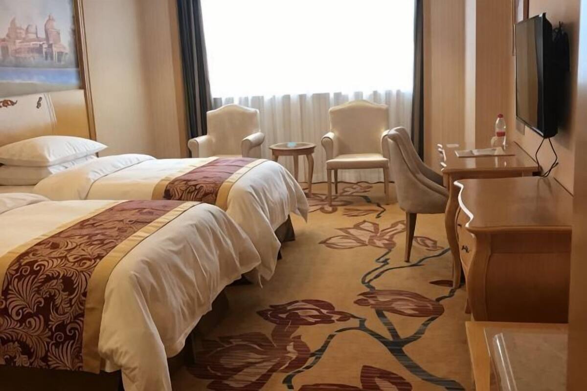 A hotel room with two beds, a desk, a chair, a TV, and a window with curtains.