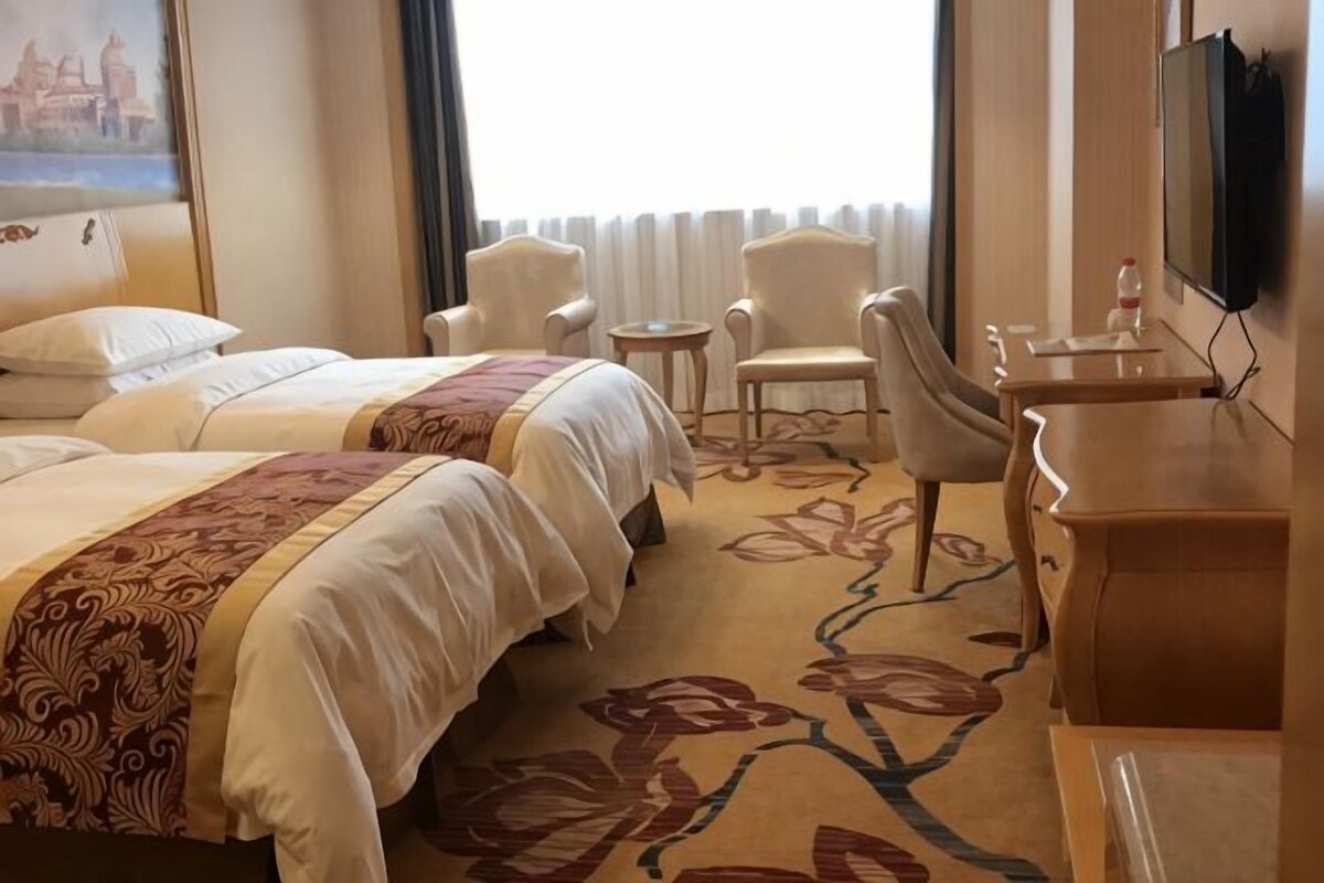 A hotel room with two beds, a desk, a chair, a TV, and a window with curtains.