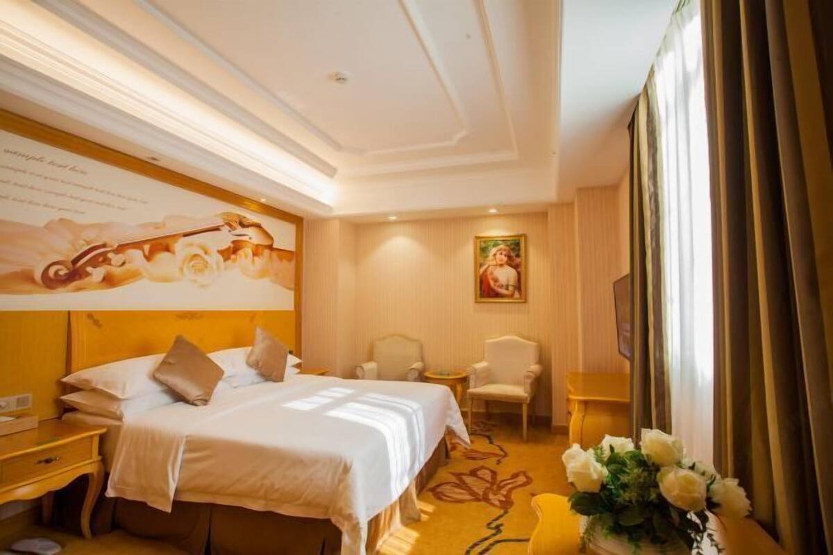 A hotel room with a large bed, two chairs, a small table, and a painting on the wall.