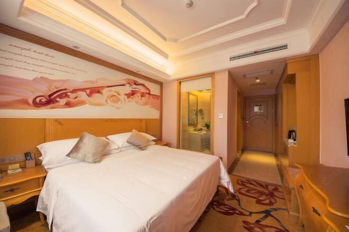 A hotel room with a large bed, a nightstand, a dresser, and a wall with a floral mural.