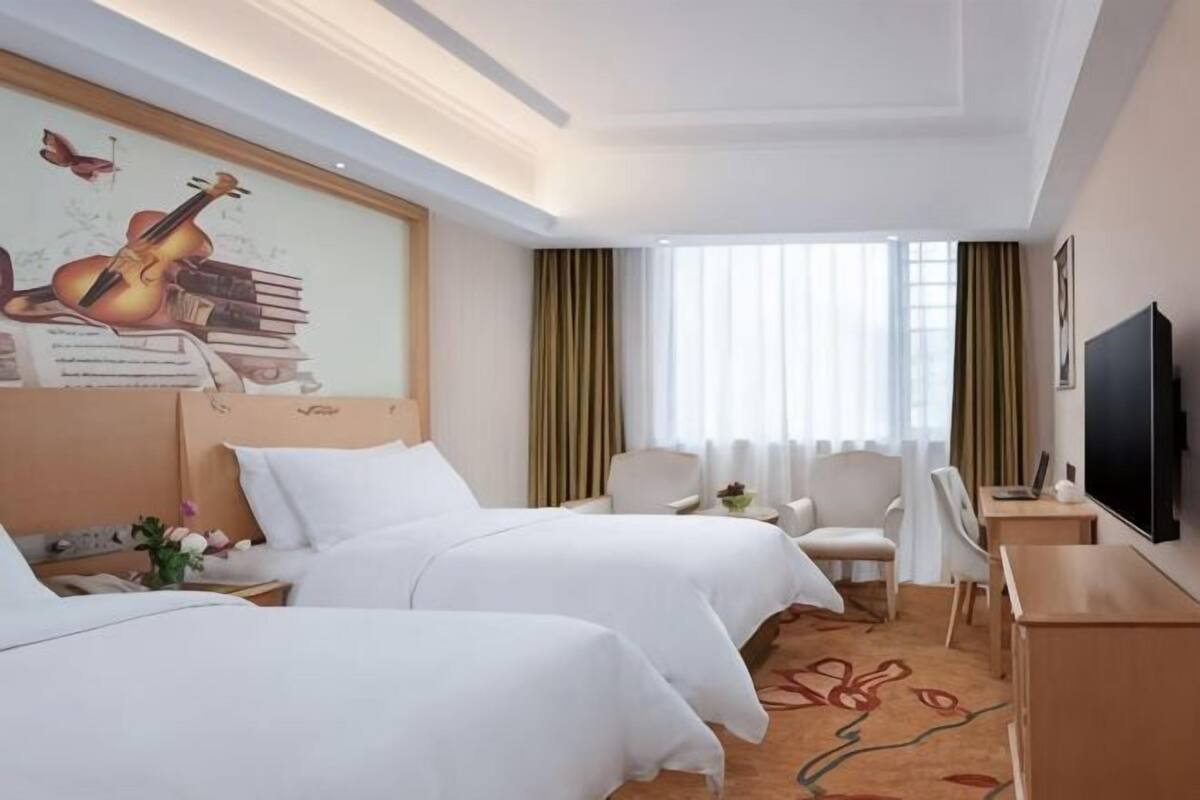 A hotel room with two beds, a desk, a chair, a TV, and a window with curtains.