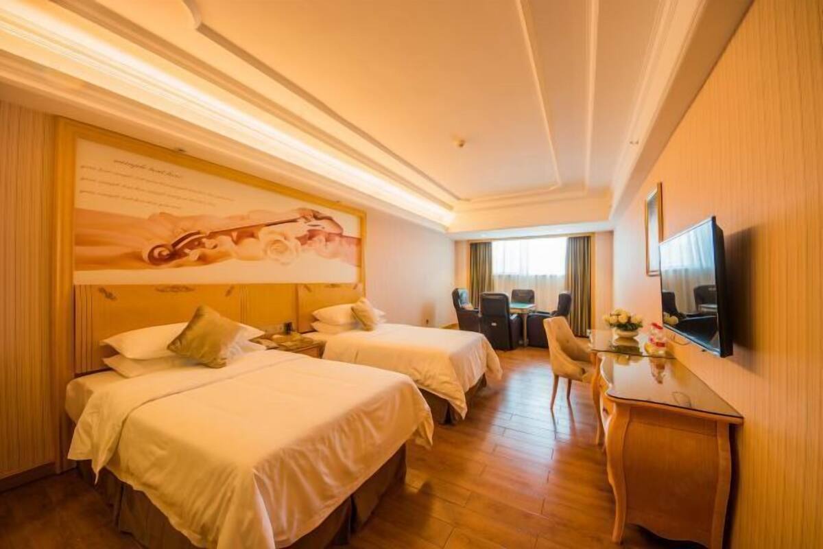 A hotel room with two beds, a desk, a chair, a television, and a large painting on the wall.