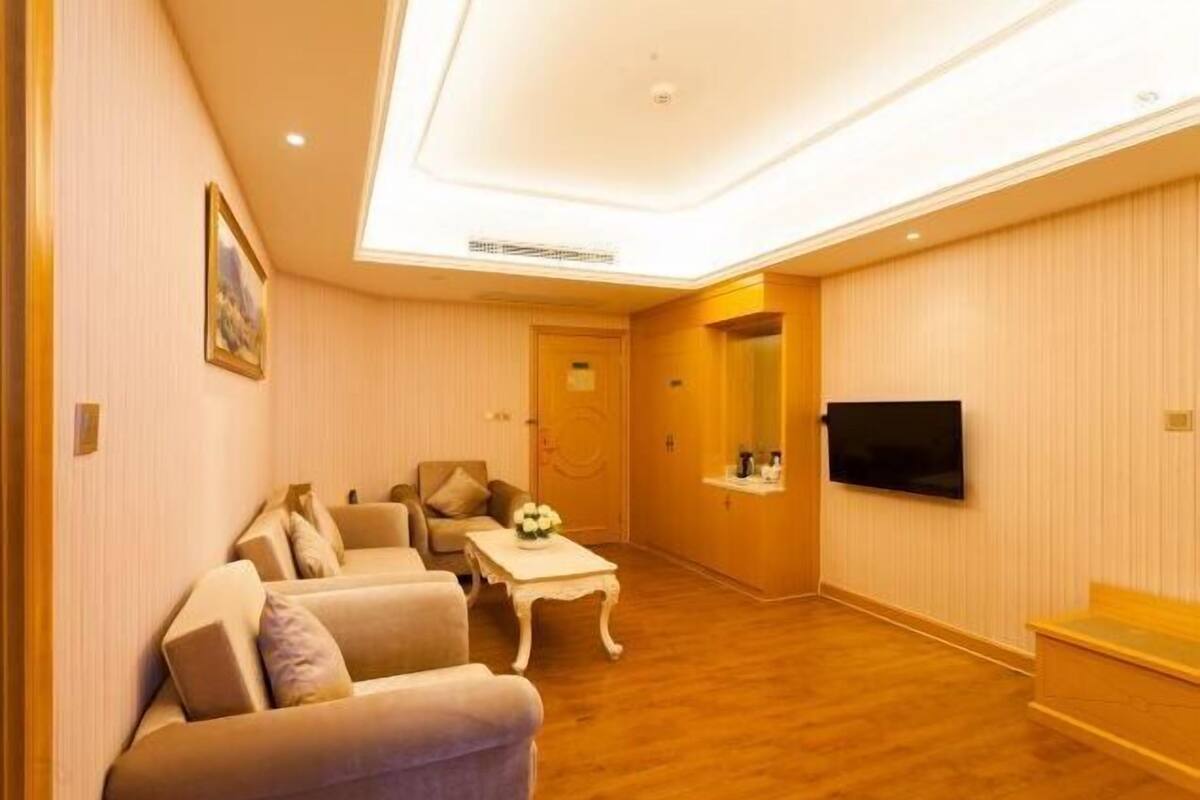 A hotel room with a sofa, a small table, a television, and a wooden floor.