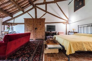 Una habitación rústica con vigas de madera a la vista, un sofá rojo, una cama amarilla y una alfombra estampada.