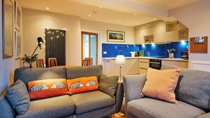 Ein modernes Wohnzimmer mit einem grauen Sofa, orangefarbenen und grauen Kissen, einem Couchtisch und einem Essbereich mit Stühlen und Tisch.