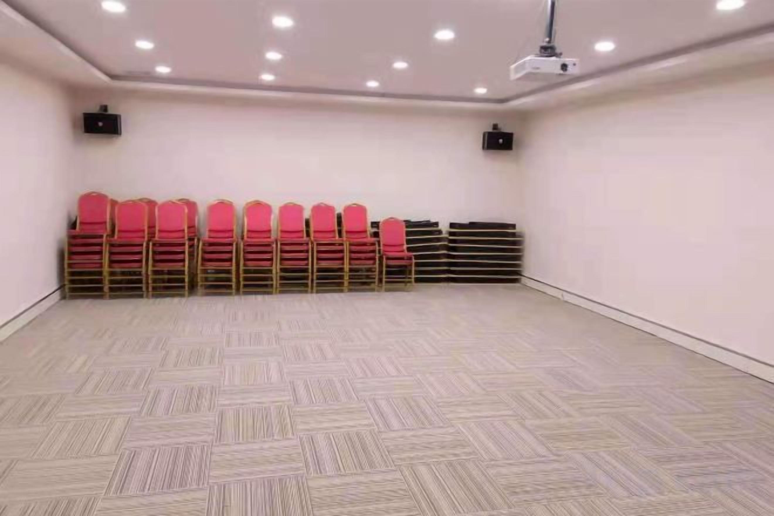 A conference room with a patterned floor, rows of red chairs, and ceiling-mounted projectors.