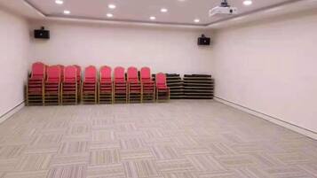 A conference room with a patterned floor, rows of red chairs, and ceiling-mounted projectors.