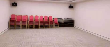 A conference room with a patterned floor, rows of red chairs, and ceiling-mounted projectors.