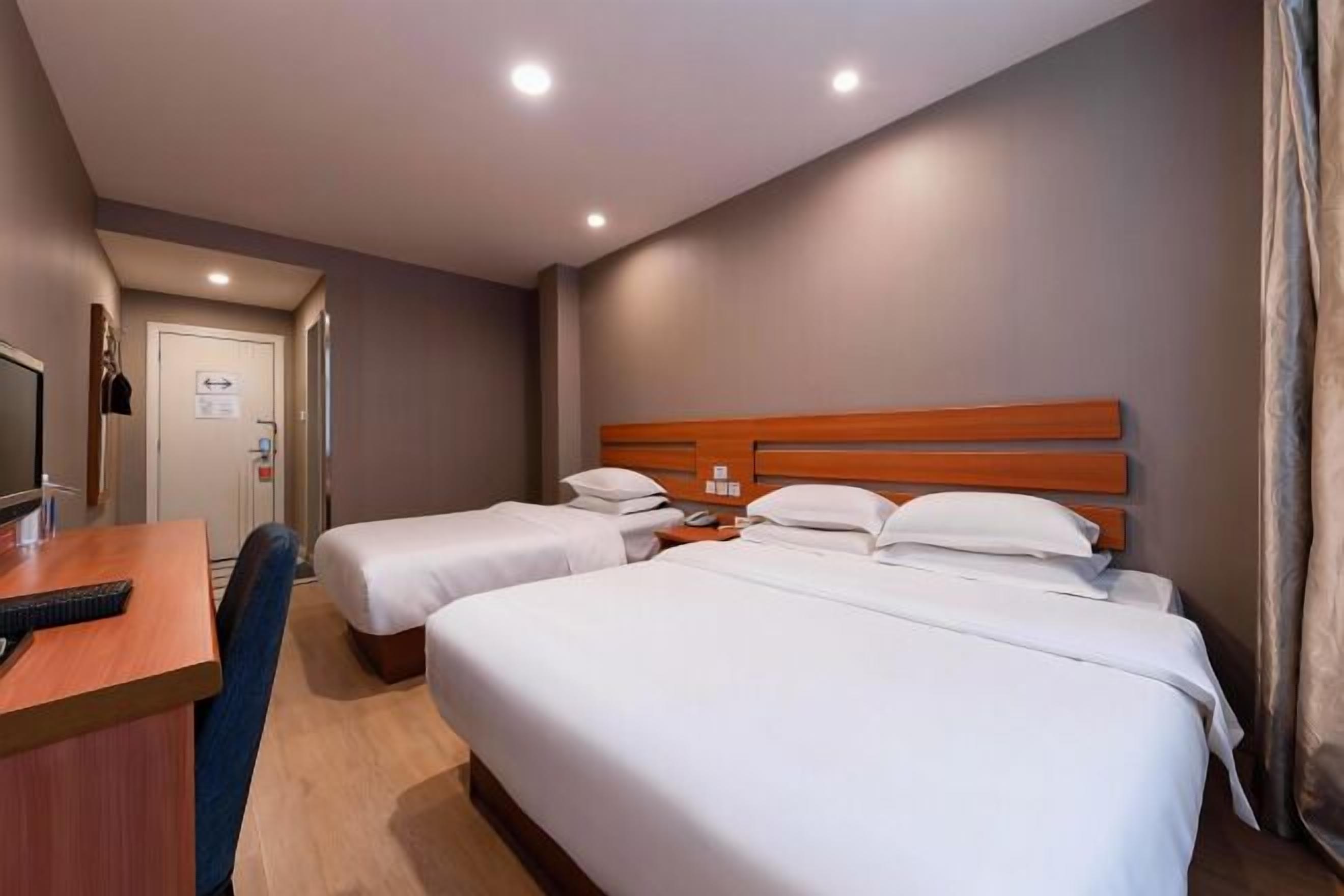 A hotel room with two single beds, a desk with a chair, a television, and a door with a sign.