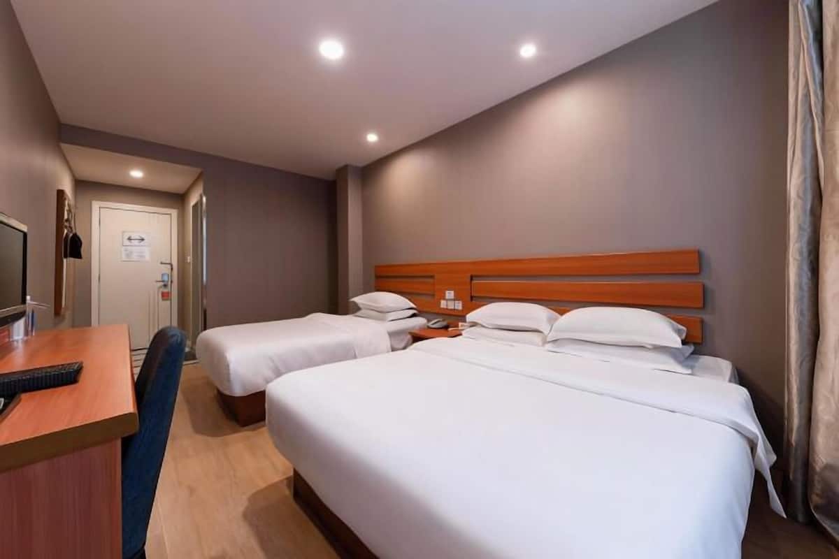 A hotel room with two single beds, a desk with a chair, a television, and a door with a sign.