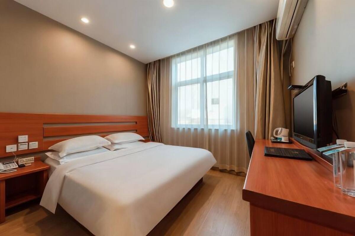 A hotel room with a bed, a desk with a computer, a TV, and a window with curtains.