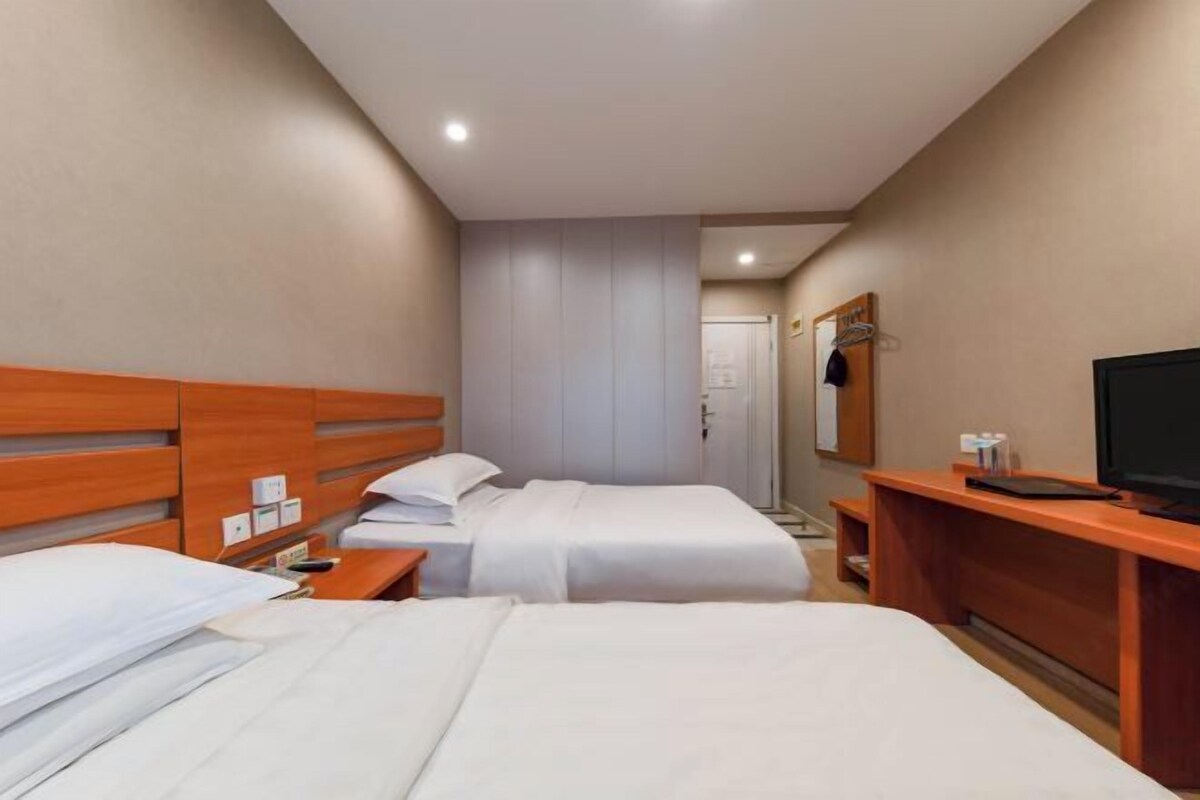 A hotel room with two beds, a TV, a desk, and a mirror.