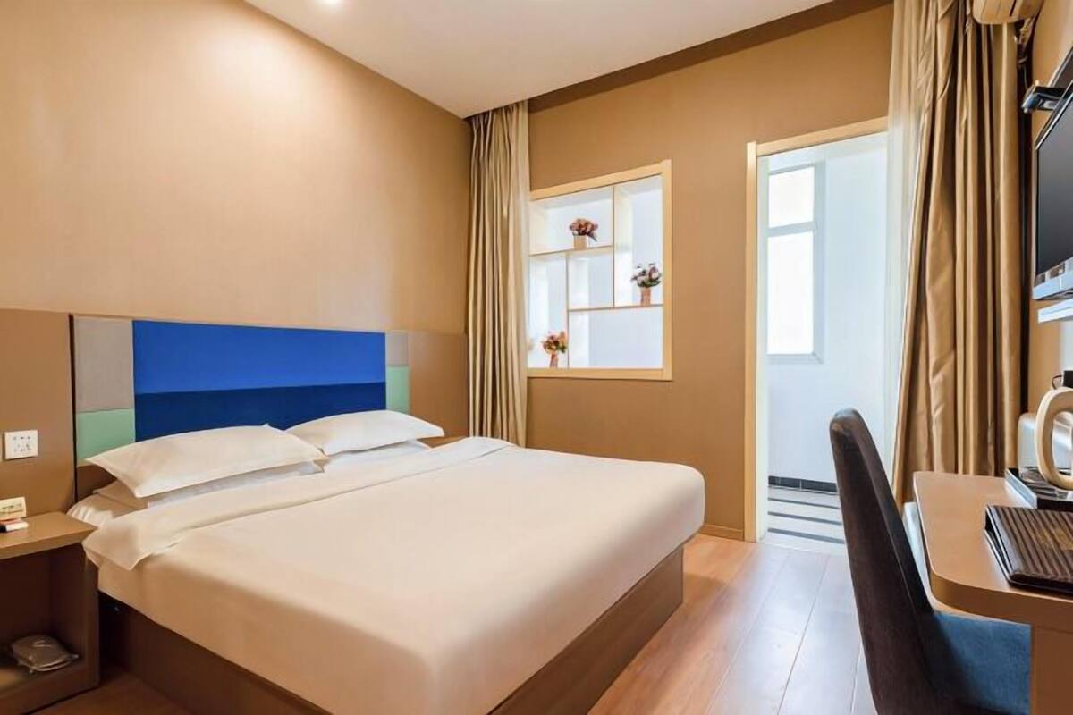 A hotel room with a bed, a desk with a chair, a television, and a window with curtains.