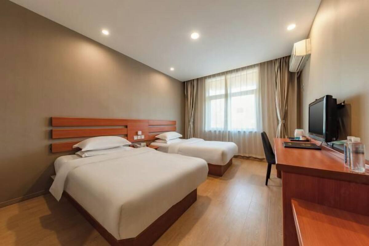 A hotel room with two beds, a desk, a television, and a window with curtains.