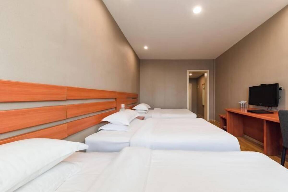 A hotel room with three single beds, a wooden headboard, a television, and a desk with a chair.