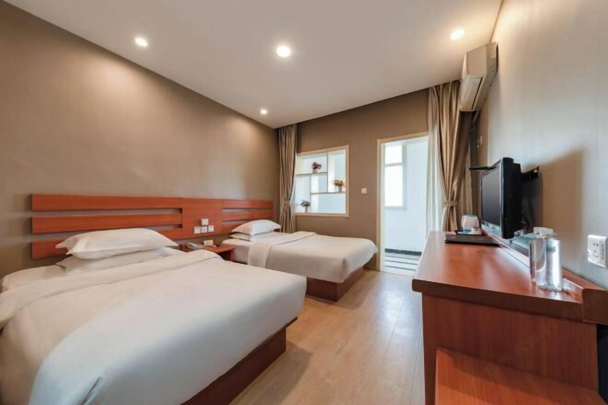 A hotel room with two beds, a wooden headboard, a desk with a TV, and a window with curtains.