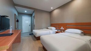 Habitación de hotel con dos camas, un escritorio, un televisor y una puerta que da a un pasillo.