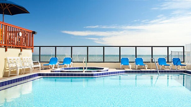 Zona de piscina con sillas azules y vista al océano.