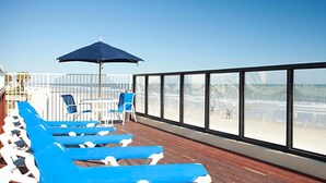 Terraza con sillones reclinables azules y una mesa, con vista a la playa.