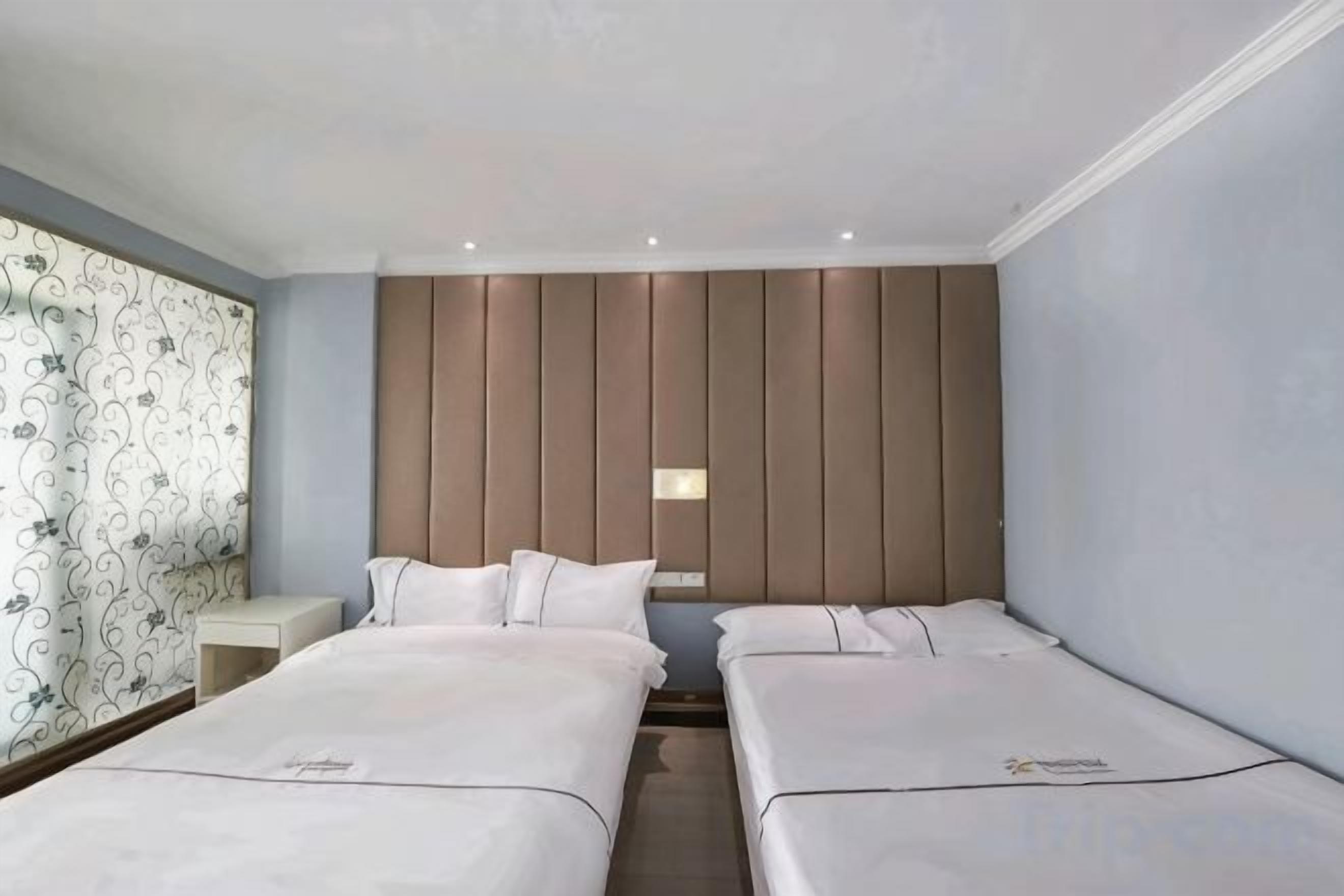 Une chambre d’hôtel avec deux lits, une table de chevet, une lampe fixée au mur et un papier peint à motifs sur un des murs.