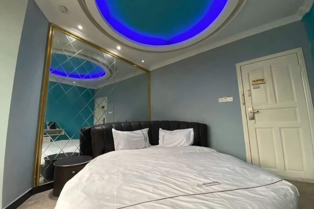 Une chambre avec un grand lit, un miroir, une porte blanche et un plafond doté d’un éclairage bleu.