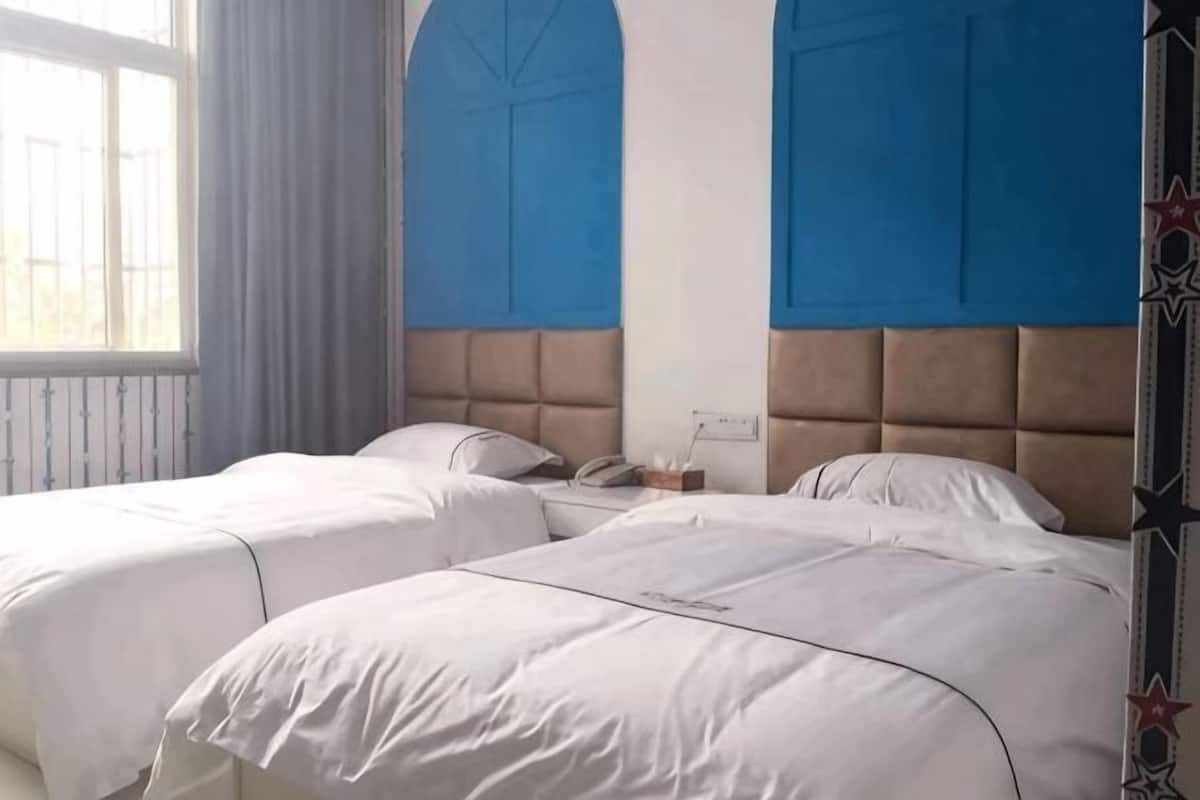 Une chambre d’hôtel avec deux lits, une fenêtre avec des rideaux et un mur d’accent bleu.
