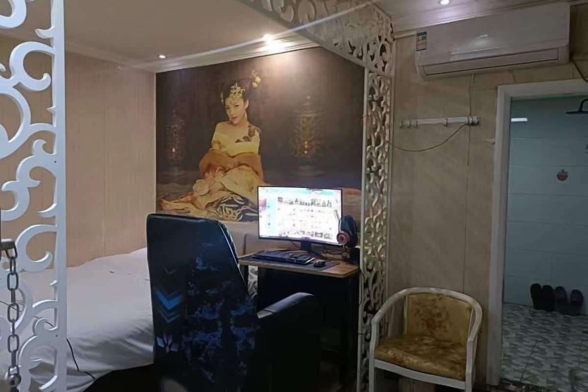 Une chambre d’hôtel avec un lit, un bureau avec un ordinateur, une chaise, un mur décoratif et une porte près de l’entrée, avec des chaussures à côté.