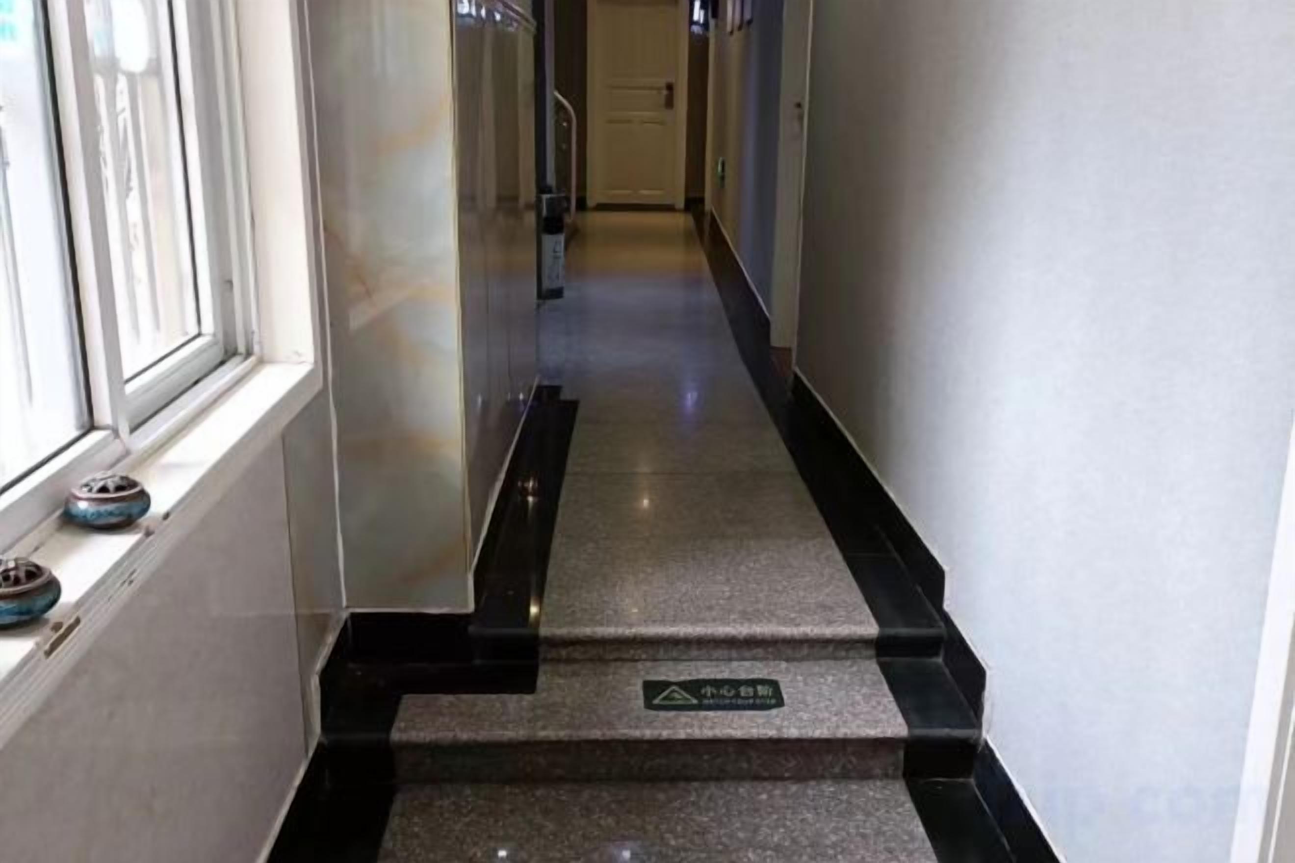 Um corredor com corrimão preto, placa indicando área para não fumantes e janela com persianas.