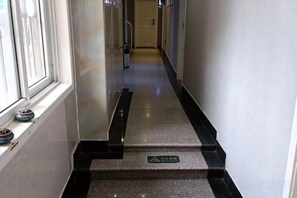 Un couloir avec une rambarde noire, un panneau indiquant une zone non-fumeur et une fenêtre avec des stores.