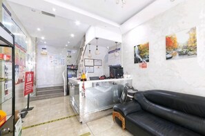 A reception area with a counter, a black leather sofa, and a staircase leading to the upper floor. - Wuwei E-sports Sunshine Holiday Hotel (Wuwei)