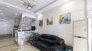 A hotel lobby with a black leather sofa, a reception desk, a kitchen area, and a refrigerator.