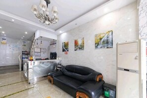 Rebedor d'hotel amb un sofà de pell negra, una taula de recepció, una zona de cuina i un refrigerador.