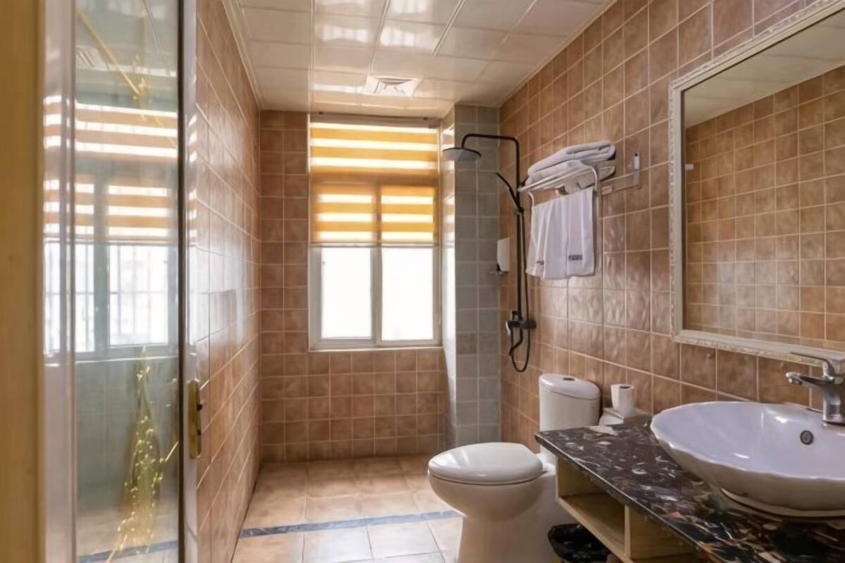 Une salle de bain équipée de toilettes, d’un lavabo, d’une douche et d’une fenêtre avec des stores.