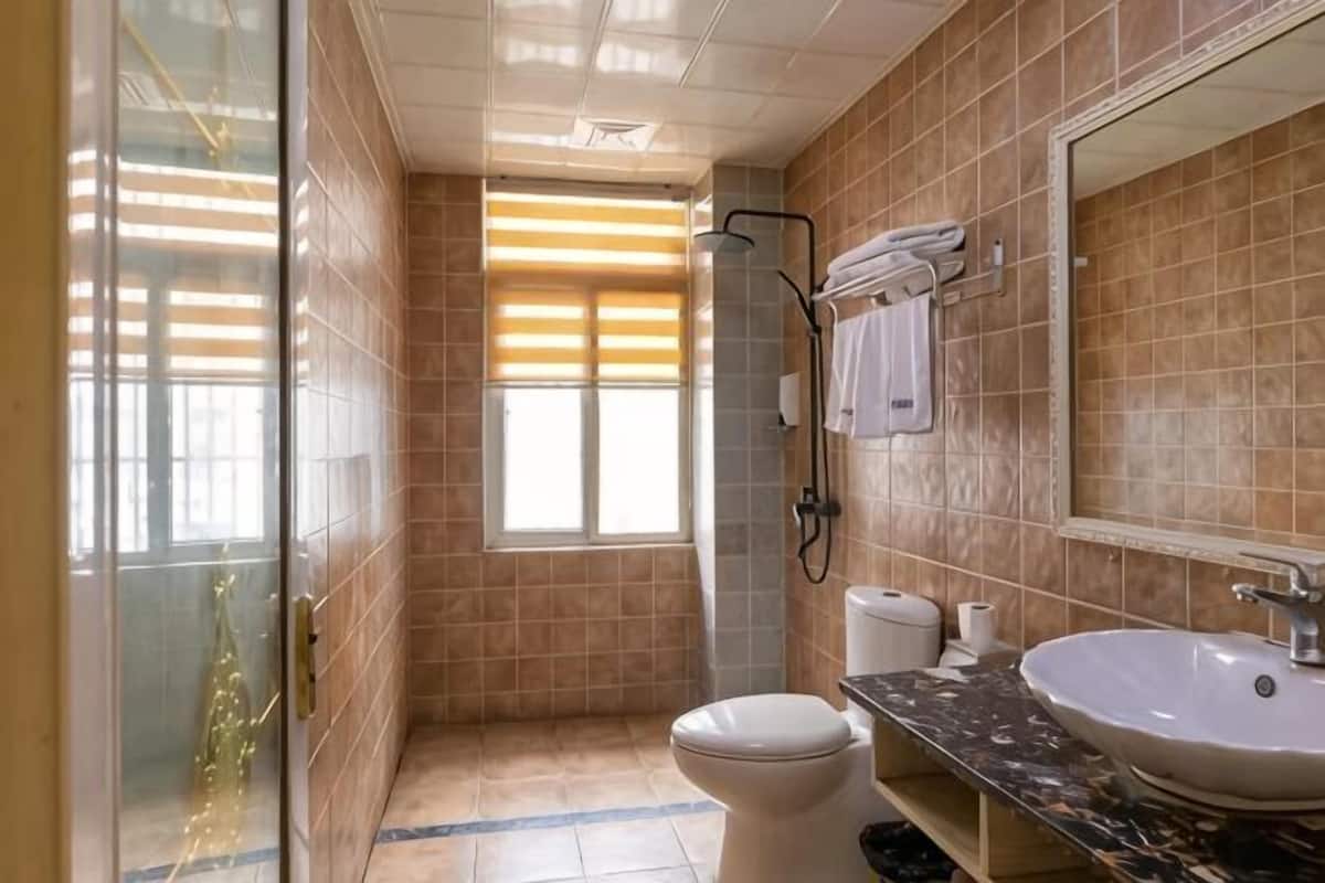 A bathroom with a toilet, sink, shower, and a window with blinds.
