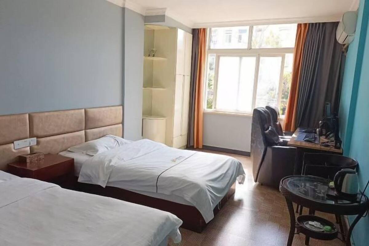 Une chambre d’hôtel avec deux lits, un bureau, une chaise et une fenêtre avec des rideaux.
