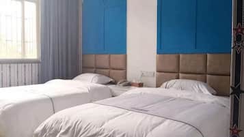 Quarto de hotel com duas camas, uma janela e parede azul.